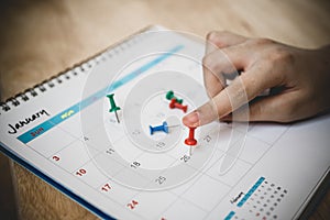 People's hand press red thumbtack on white calendar to marked important date