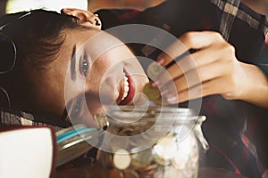 People`s hands putting money coins into the glass bottle.