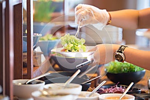 People are scooping vegetable salad from chafing dishes on the buffet table