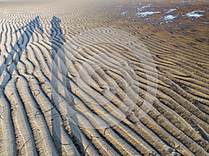 People shadows reflecting in sand ripples at Low Tide with water