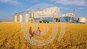People shaking hands in a wheat field, farmer`s agreement. Grain elevator terminal on background. Agriculture agronomist