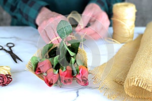 close up of causcasian florist woman wrapping red rosebuds in burlap