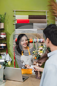 People, shopping, sale, floristry and consumerism concept - happy smiling florist woman making bouquet for and man or customer at