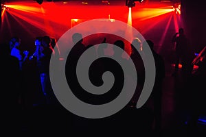 People silhouettes on dance floor of night club at the concert under red spotlights