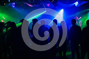 People silhouettes on dance floor of night club to laser projectors