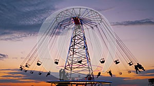 People silhouettes ride on the chained carousel against twilight sky in evening