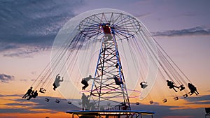 People silhouettes ride on the chained carousel against twilight sky in evening