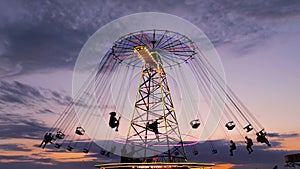 People silhouettes ride on the chained carousel against twilight sky in evening