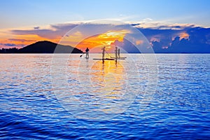 People silhouettes stand SUP paddle boarding, sea sunset beach, active young man woman surfing paddling board, ocean sunrise