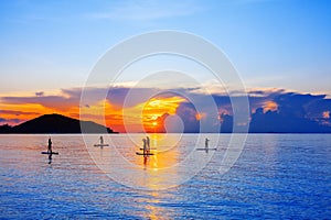 People silhouettes stand SUP paddle boarding, sea sunset beach, active young man woman surfing paddling board, ocean sunrise