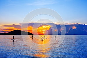 People silhouettes stand SUP paddle boarding, sea sunset beach, active young man woman surfing paddling board, ocean sunrise