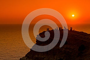 People silhouettes on the sunset on the cliff over the sea