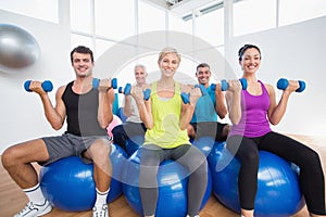 People sitting on balls and lifting weights in fitness club