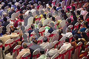 People are sitting on chairs and watching a function in a hall