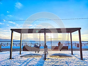 People sitting close on a swing under a clear, cold sky in spring. Couple Enjoying a Winter Sunset on a Park Swing on