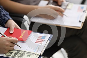 People sitting in line with documents for obtaining American visa and money closeup