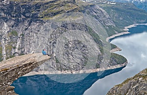 People sitting on Trolltunga rock and looking at Norwegian mountain landscape
