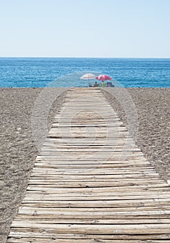 Wooden path leading to people sitting on beach under umbrellas