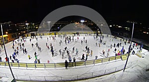 People skate on big ice rink at dark winter night.