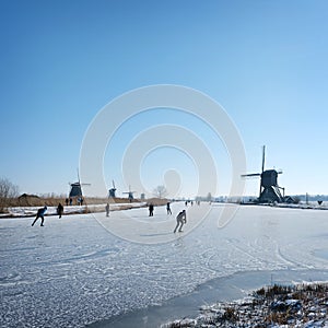 people skate on the ice near kinderdijk with al lot of windmills in holland on sunny winter day