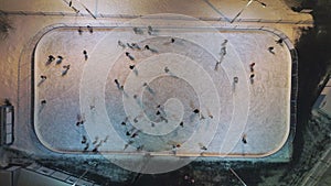 People are skating on illuminated ice rink in the evening. Aerial vertical top-down view