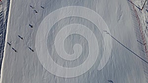 People skiing down a steep slope at a ski holiday resort in the mountains. Top down aerial view.