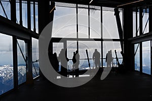 People with skis as silhouettes wait in the ropeway or cable car station for the gondola on the Zugspitze, the highest mountain of