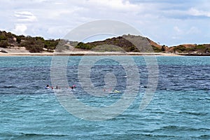 People snorkeling on a shallow coral reef near a sand island