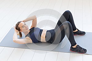 People, sport and fitness concept - young fitness woman doing abs crunch exercise on floor at home
