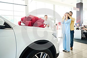 People stand in front of car with gift bow on hood