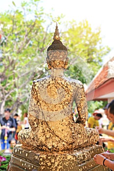 People sticking the gold foil sheet on back Buddha statue for respect