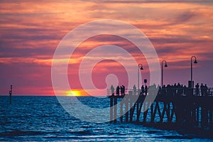 People strolling along the Glenelg Jetty at sunset