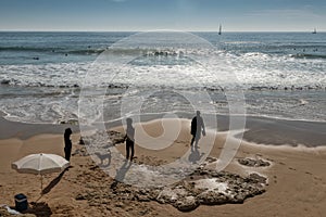 people strolling on the carcavelos beach with surfers and boat