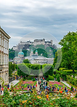 People are strolling through Mirabell Gardens with the old historic Fortress Hohensalzburg in the background in Salzburg