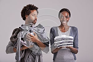 People, studio and pile of clothes in hand for laundry day, wash and couple cleaning together. Woman, happy and neat