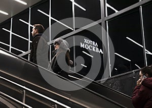 People on subway escalator with lights reflection and hotel Moscow neon sign