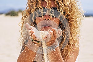People in summer holiday vacation concept - young pretty curly blonde woman blow sand at the beach in a sunny day - focus on hands