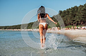 young woman in bikini swimsuit running on beach