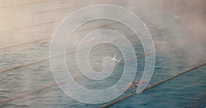 People swim in a outdoor swimming pool early in the morning. Fog over the water and training sportists for competition