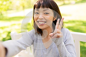 Happy asian woman taking selfie and showing peace