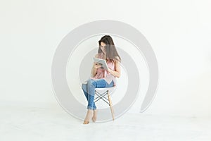 People, technology and education concept - young student woman sitting on a chair and using a tablet on white background