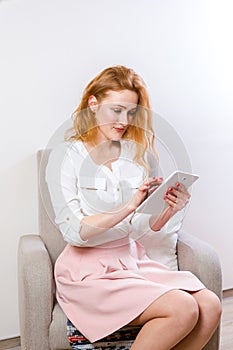 People, technology and education concept - young student woman sitting on a chair and using a tablet on white background