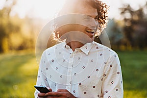 People, technology and lifestyle concept. Close up portrait of cheerful handsome smiling male with curly hair walking in the park