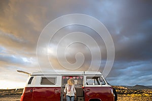 People travel and enjoy vanlife adventure lifestyle. Standing woman against a red classic vintage van. Beautiful sunset colors sky