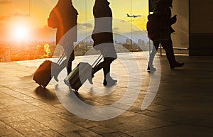 people and traveling luggage walking in airport terminal building with sun set sky at urban scene and air plane flying background