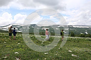 People trekking across alpine meadow of Lago-Naki plateau