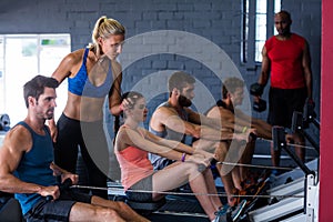 People using rowing machine with fitness instructor in gym