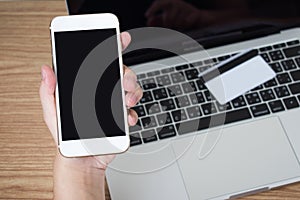 People are using smartphones to pay via a credit card placed on a laptop on a wooden table. Financial concept