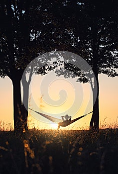 People on vacation. A girl`s silhouette in a hammock between trees. A hammock in the background of the sunset.