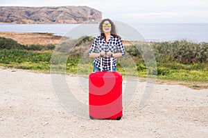 People, vacation and travel concept - beautiful young woman standing with suitcase on background the sea